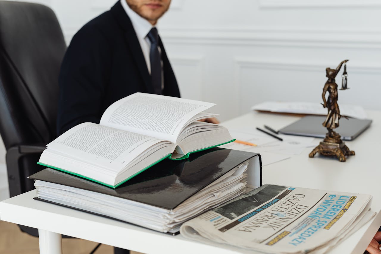 gallery-1 A lawyer sitting at a desk with legal books, documents, and a newspaper, embodying professionalism.
