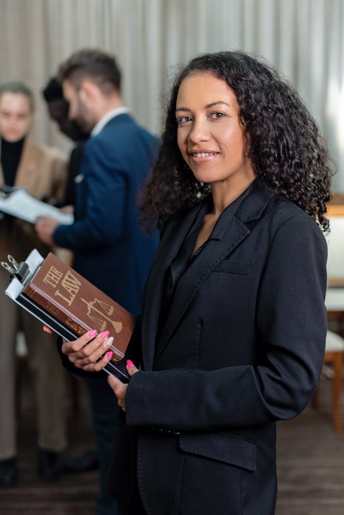 gallery-6 African American female lawyer holding a law book in an office setting, showcasing professionalism and legal expertise.